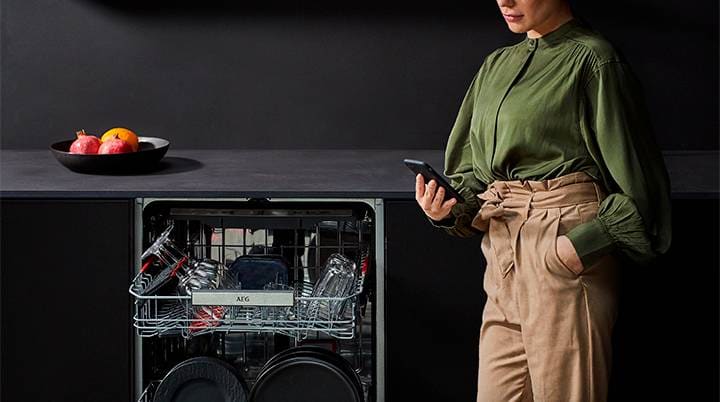 Donna in camicetta verde che usa il telefono vicino alla lavastoviglie